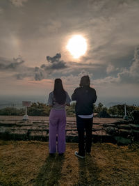 Rear view of couple standing against sky during sunset