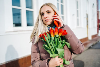 Girl at the train station is talking on a smartphone, a bouquet of tulip flowers in her hands