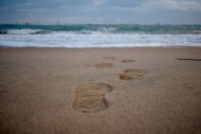 Close-up of footprints on sand at beach against sky