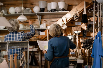 Rear view of female coworkers examining lighting equipment on shelves in hardware store