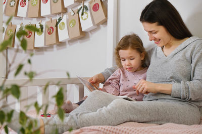 Mather with toddler child reading book or photo album on christmas eve near eco advent calendar