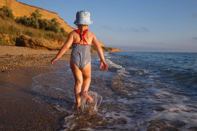 Rear view of girl running on beach against sky