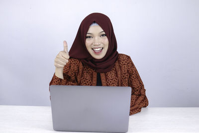 Portrait of smiling young woman using phone against wall