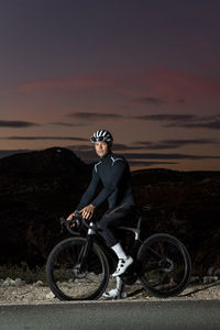 Cyclist wearing protective gear with cycle near roadside at dusk