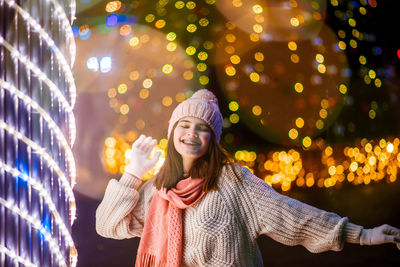 Portrait of smiling young woman holding umbrella at night