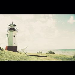 Lighthouse on beach against cloudy sky