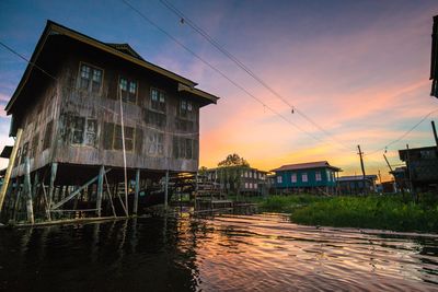 Buildings by river against sky at sunset