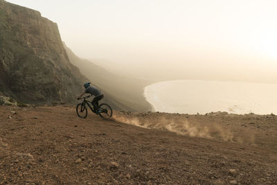 Man riding bicycle on mountain against sky