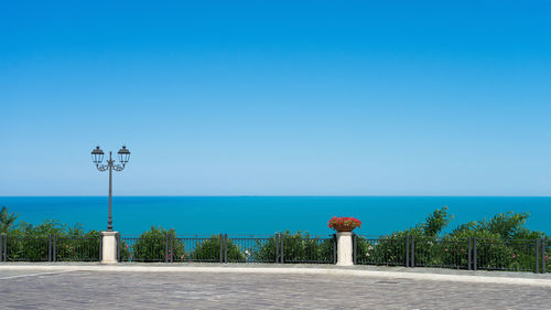 Street light by sea against clear blue sky