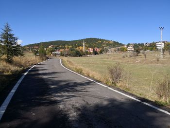 Road amidst trees against clear blue sky