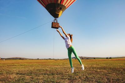 Full length of girl  jumping to catch hot air balloon on field against sky