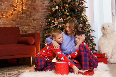 Happy family mother with sons on christmas morning in pajamas near christmas