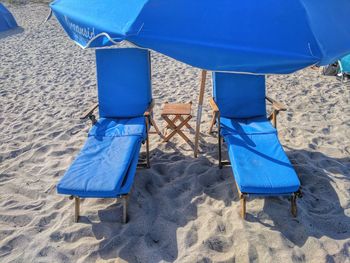 High angle view of blue lounge chairs and parasol at sandy beach