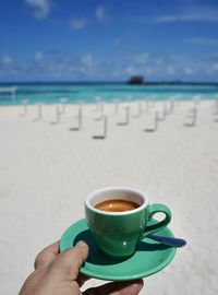 Cropped hand holding coffee on beach