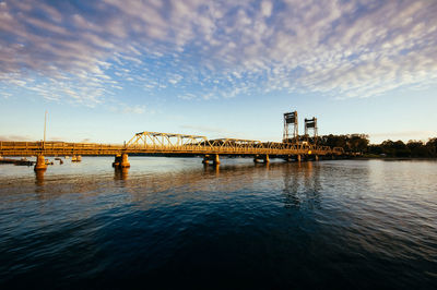 Bridge over river against sky at sunset