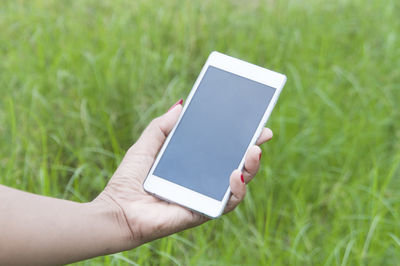 Female hand holding mobile phone against grassy field