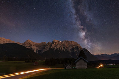 Light trails on road with mountains in background against star field