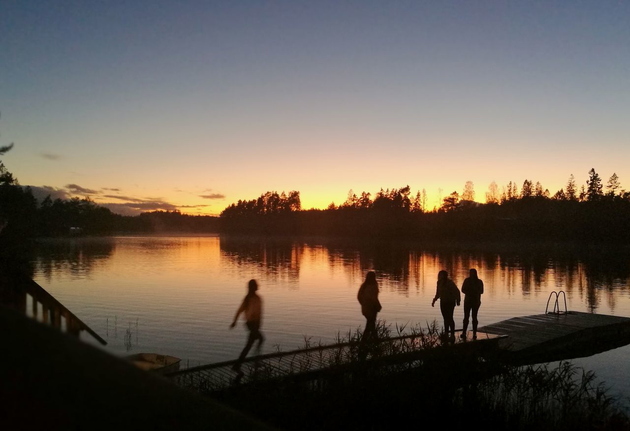 sunset, silhouette, nature, lake, leisure activity, tree, water, real people, reflection, togetherness, standing, men, lifestyles, beauty in nature, outdoors, tranquility, sky, scenics, full length, playing, boys, friendship, sports team, people, adult, day