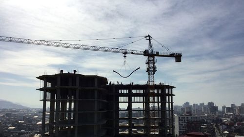 Crane over incomplete building in city against sky