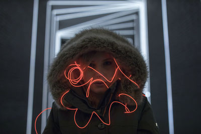 Woman in hooded clothing with light painting standing against illuminated lights