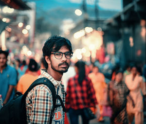 Portrait of young man standing on illuminated street at night