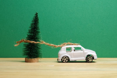 Close-up of small christmas tree tied with toy car on wooden table against green background