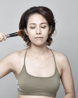 Woman applying make-up with brush against gray background