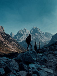 Full length of man standing on rock by snowcapped mountain against sky