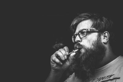 Close-up of man smoking against black background