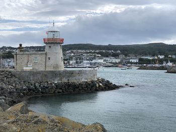 Lighthouse amidst buildings by sea against sky