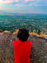 Rear view of man sitting on landscape against sky