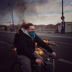 Man riding bicycle on road in city against sky