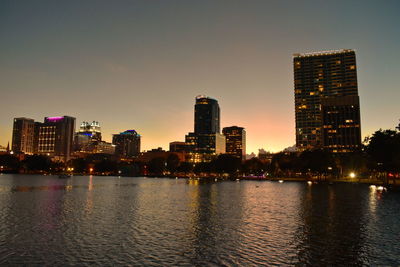 Illuminated buildings by river against sky in city