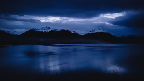 Scenic view of lake by snowcapped mountains against sky at dusk