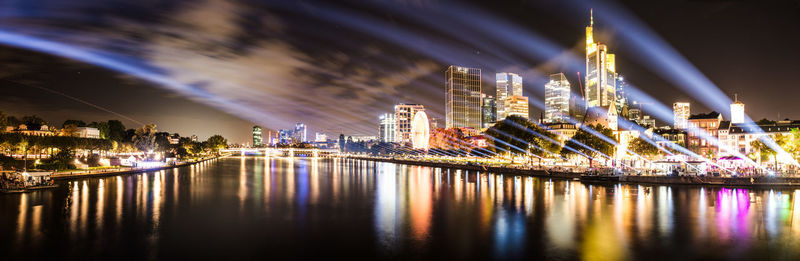 Illuminated buildings by river against sky at night