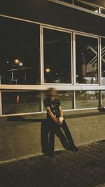 Woman photographing while sitting on window of building at night