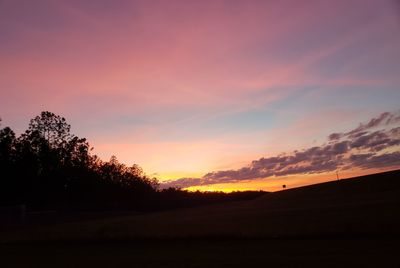 Silhouette trees on field against romantic sky at sunset