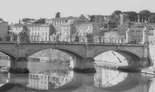 Arch bridge over river in city against clear sky