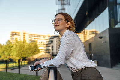 Smiling businesswoman with smart phone leaning on railing