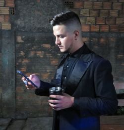 Young man looking away while standing against wall