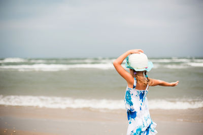 Rear view of woman standing at beach against sky