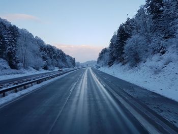 Road amidst snow covered landscape against sky