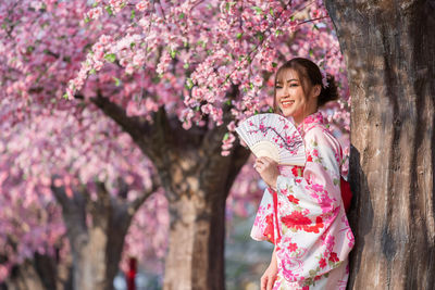 Woman standing by pink cherry blossom tree