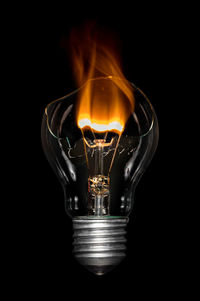 Close-up of broken light bulb burning against black background