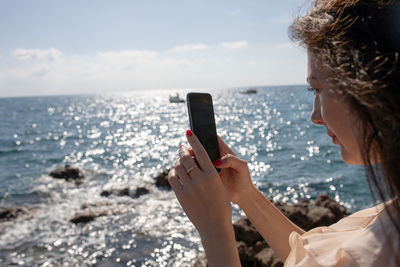 Close-up of woman photographing with mobile phone at beach against sky