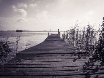Narrow wooden jetty leading to pier over sea against sky