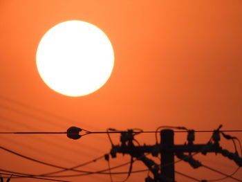 Low angle view of silhouette electricity pylon against orange sky