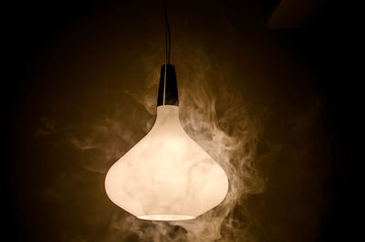 Close-up of illuminated lamp hanging against black background