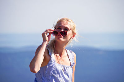 Young woman wearing sunglasses standing against sky