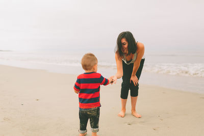 Mother and son standing at beach against sky